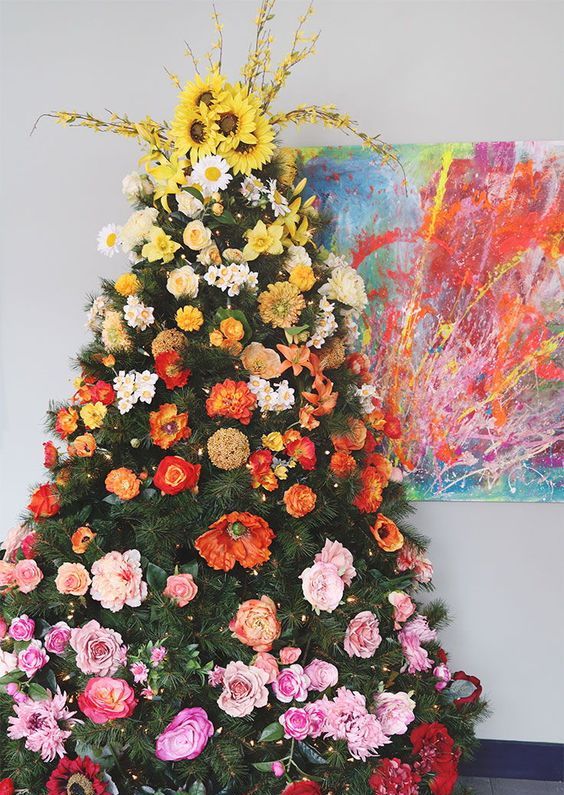 a bright ombre Christmas tree decorated with faux flowers and topped with bold faux sunflowers and blooming branches