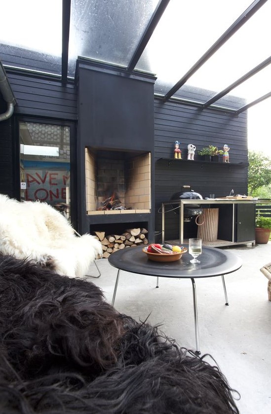 a contemporary winter terrace with a sheer roof, a fireplace with firewood, a grill table, a large coffee table and faux fur chairs around it