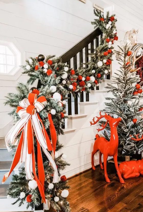 a fantastic Christmas entryway styled with red deer, a flocked tree with red and white ornaments, a lush railing garland with a large red and white bow