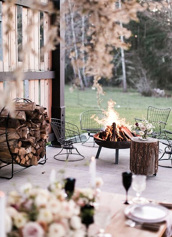 a gorgeous winter terrace with metal chairs around the fire bowl, a tree stump side table and a round metal stand with firewood
