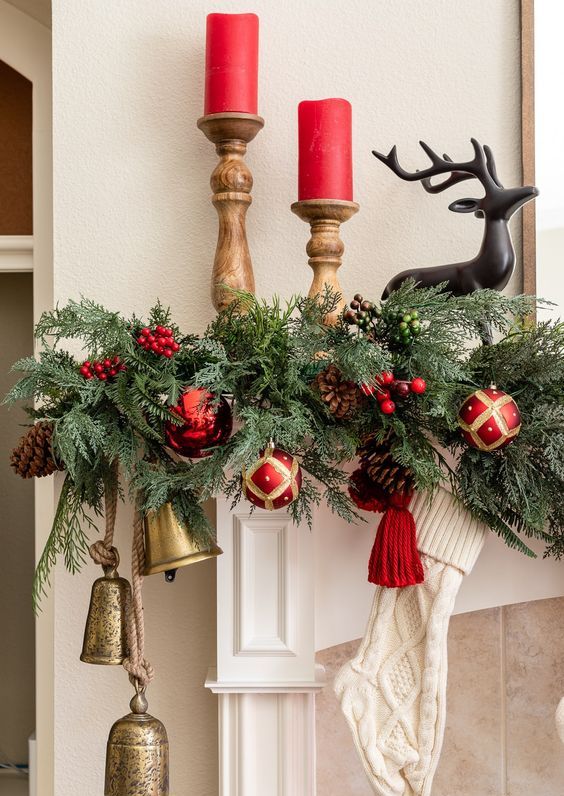 a lush and bright Christmas garland of evergreens, red ornaments, pinecones, berries and large bells is a cool decor idea for the holidays