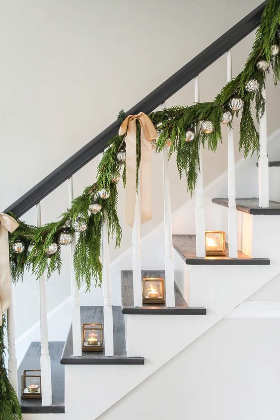 a refined holiday garland of evergreens, mercury glass ornaments, neutral bows and candles lanterns placed on steps