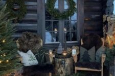 a rustic winter terrace with wooden chairs with black upholstery and pillows, a tree stump table, evergreens, a Christmas tree and candles