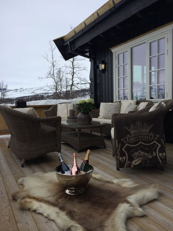 a simple and cozy winter terrace with wicker furniture, neutral upholstery and pillows, faux fur rugs and a bowl with bottles