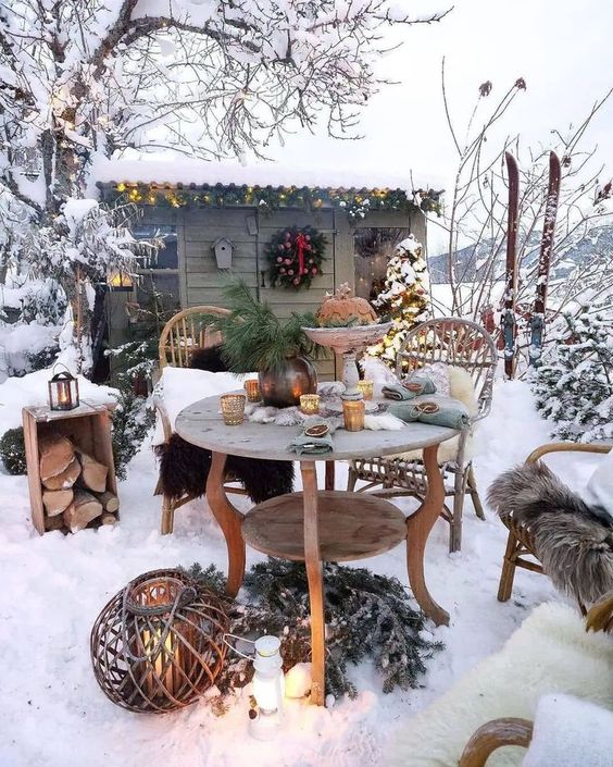 a winter patio done with vintage wooden furniture, evergreens, candle lanterns and firewood storage is a cool and cozy space