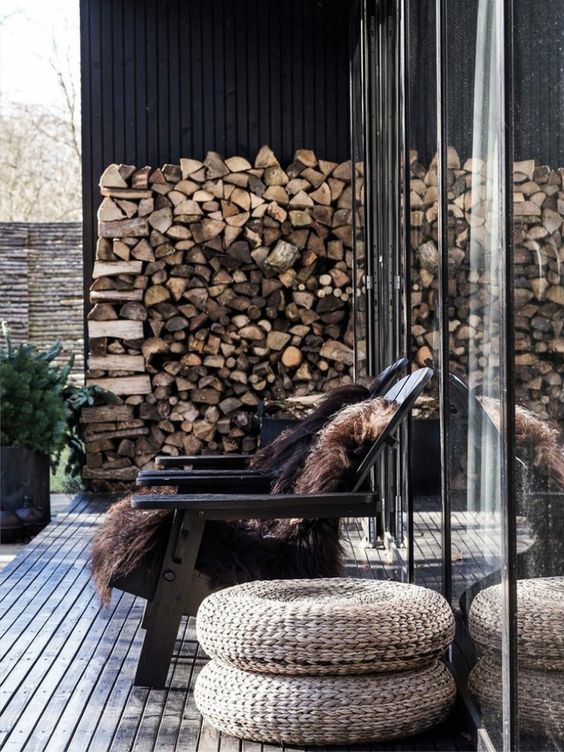 a winter terrace with black chairs and faux fur, jute poufs, a firewood stock and potted greenery is lovely