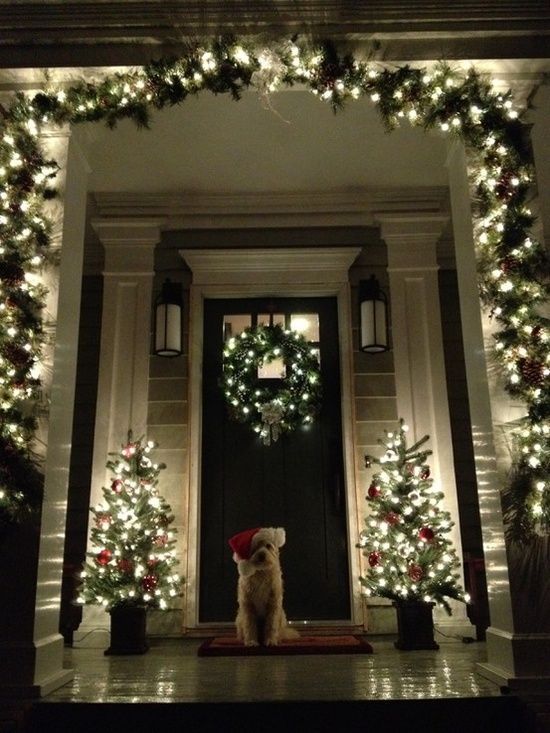 an evergreen and light garland, mini Christmas trees and a wreath make the porch very Christmassy and welcoming
