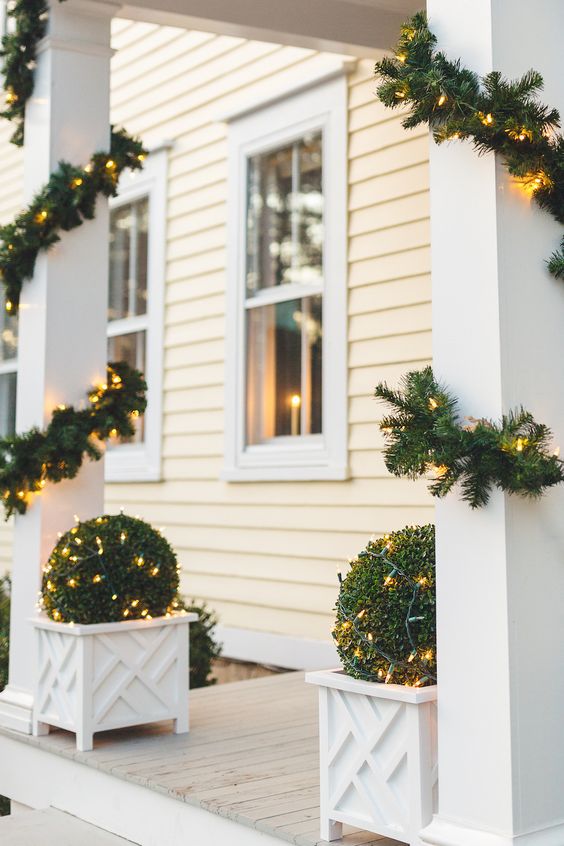 evergreen and light garlands covering the pillars and matching lit up topiaries in white planters make the space awesome