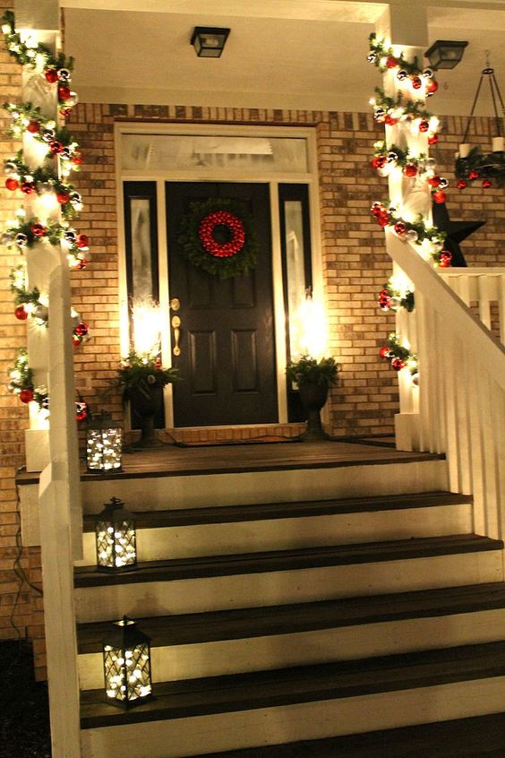 evergreen, red ornament and light garlands covering the pillars and lanterns with lights make the porch very cool and bright