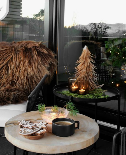 side tables wth evergreens, a mini Christmas tree, candles in dark candleholders and faux fur throws on the chairs