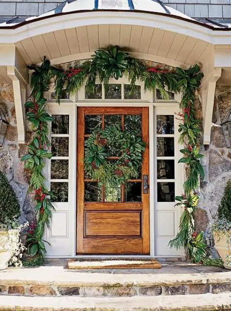 simple and natural Christmas front door styling with an evergreen garland with red blooms and a matching large wreath on the door