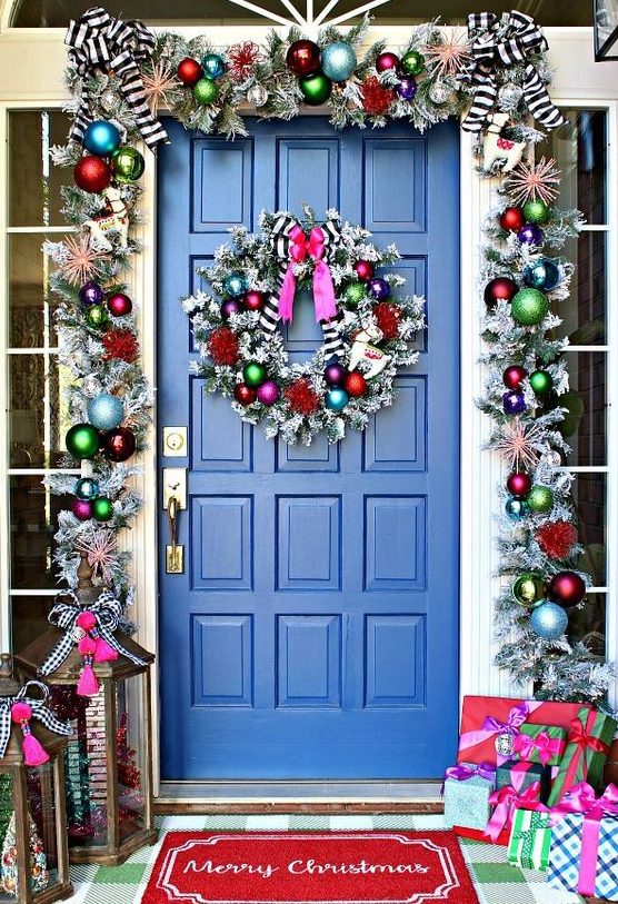 super bright Christmas front door decor with a silver garland with colorful ornaments, striped bows and a matching wreath plus colorfil gift boxes