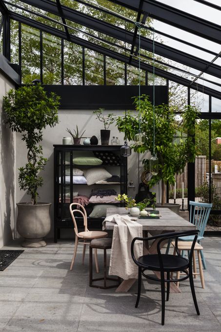 a Scandinavian sunroom with mismatching chairs, a wooden table and a large storage unit, potted greenery
