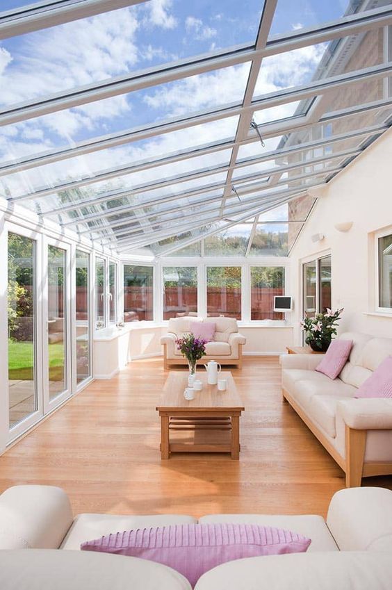 a bright contemporary attic sunroom with neutral sofas and pink pillows, a wooden table and some teaware is very welcoming