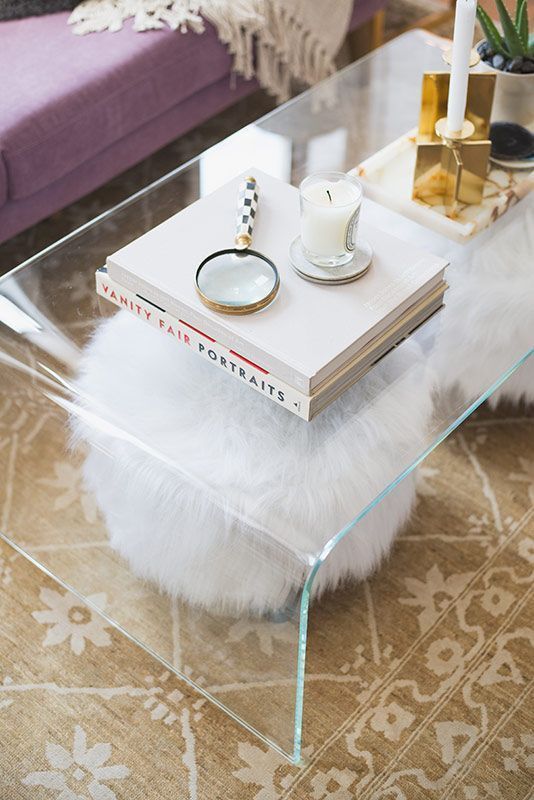 a clear acrylic coffee table with two faux fur stools under it   they are seen, which makes them part of the decor