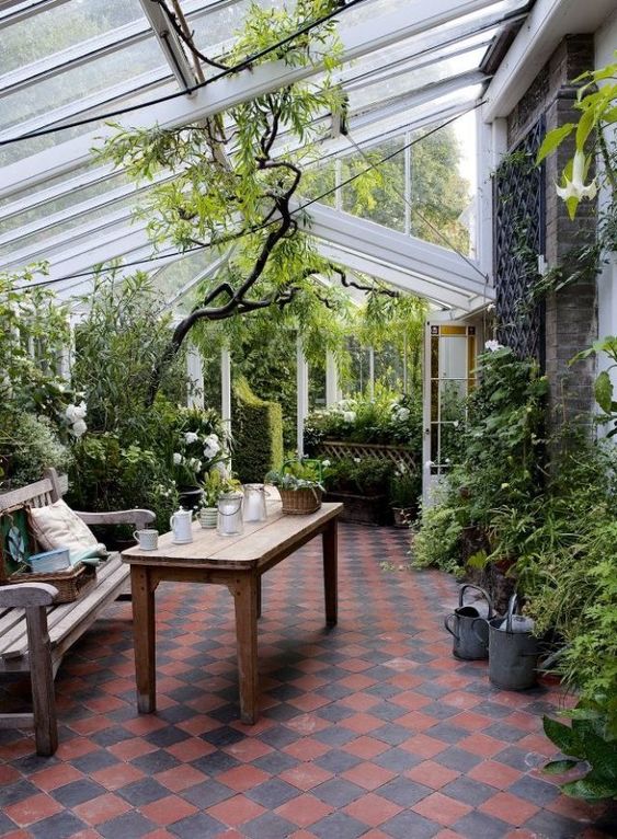 a conservatory with lots of greenery and blooms, wooden furniture and candle lanterns