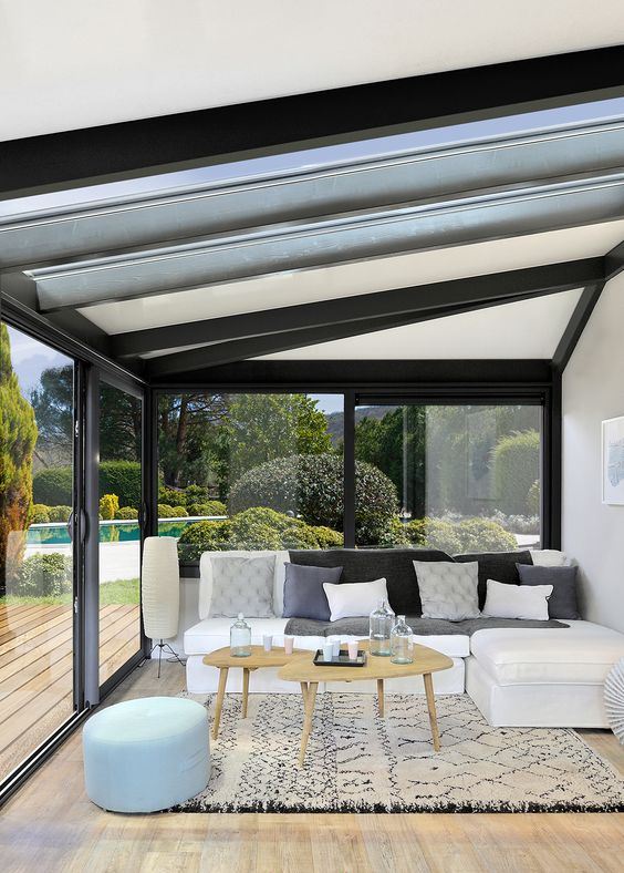 a contemporary sunroom with a sectional, some rugs, tables and ottomans and much shunshine