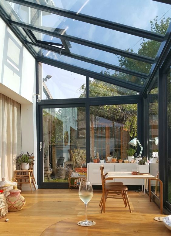 a gorgeous attic sunroom and home office with a desk, a chair, some plants on stands and a cabinet plus baskets