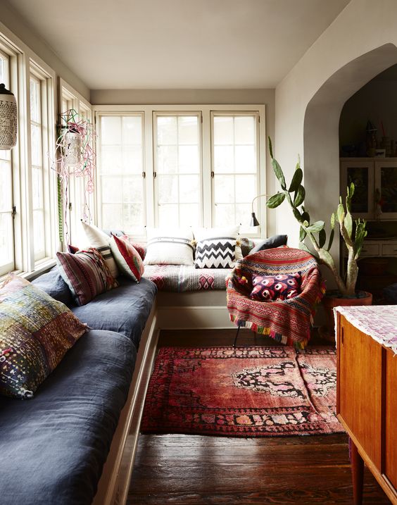 a lovely boho sunroom space with a large built in sofa and colorful upholstery and pillows, a bold printed rug and a chair