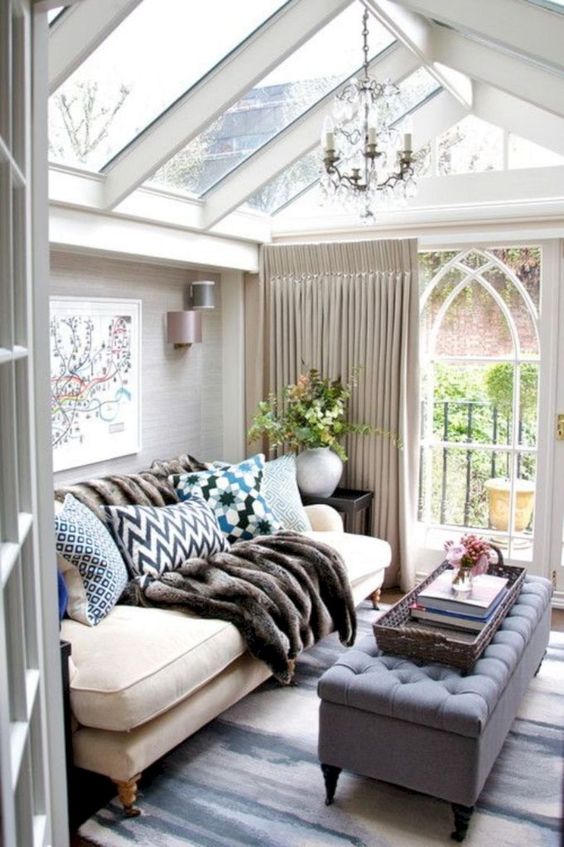 a small refined sunroom with elegant furniture, lots of pillows, a fir throw, a vintage chandelier and neutral curtains