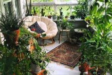 a small yet cozy boho sunroom turned into an orangery, with lots of potted plants and greenery, a round chair and some stools
