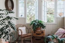 a small yet pretty boho sunroom with rattan and wicker furniture and accessories, potted plants, a basket with a lid and shutters