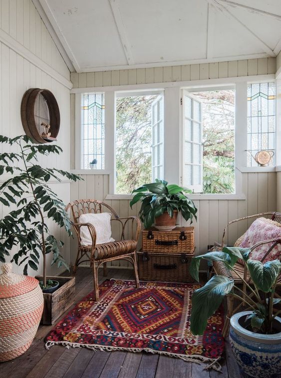 a small yet pretty boho sunroom with rattan and wicker furniture and accessories, potted plants, a basket with a lid and shutters