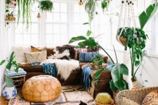 a stylish boho sunroom with a brown sectional, colorful pillows, a rug, potted plants, a leather pouf and a statement cactus