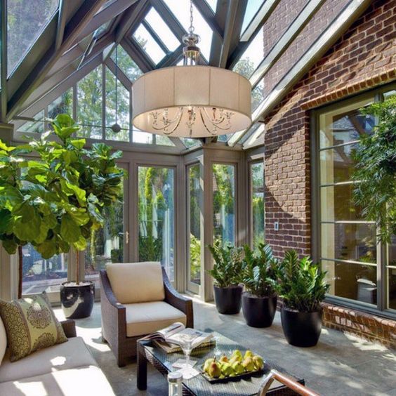 a stylish mid-century modern sunroom with elegant dark furniture, potted greenery, a pdant lamp and much light