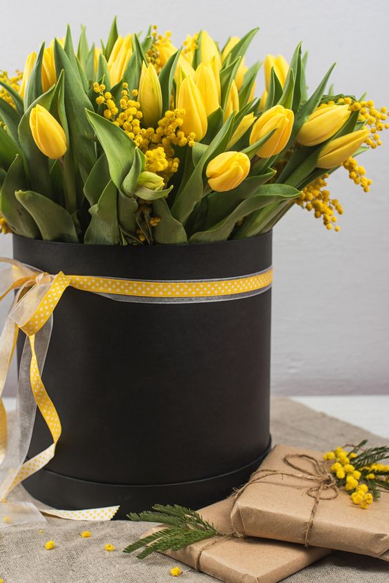 a tall black cylinder with yellow tulips and mimosa blooms is a cool idea to bring a contrasting touch to the space