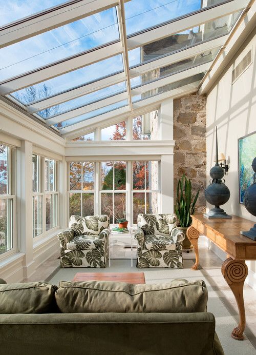 a tropical vintage sunroom with tropical leaf chairs, a green grey sofa, a wooden table and some plants
