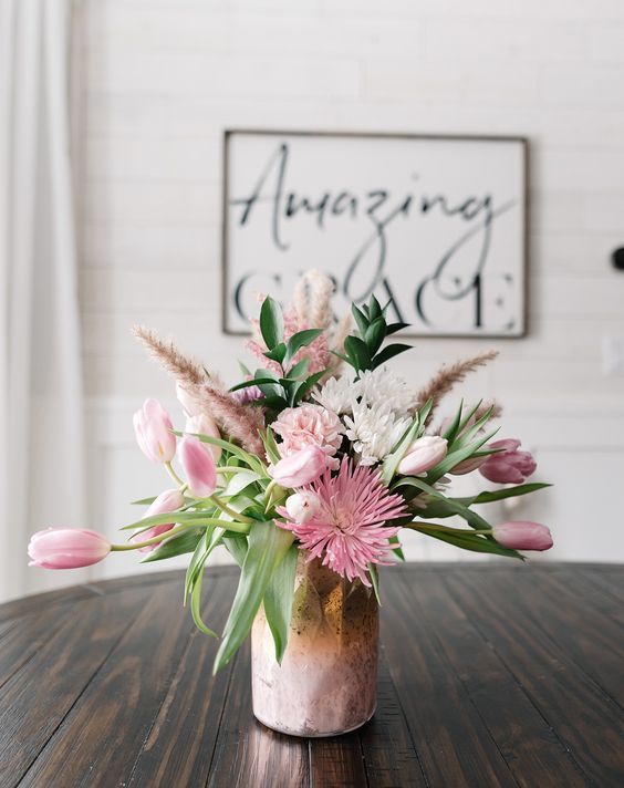 a very simple and lovel spring floral arrangement with a pink vase, pink and white blooms, greenery and pink grasses is wow