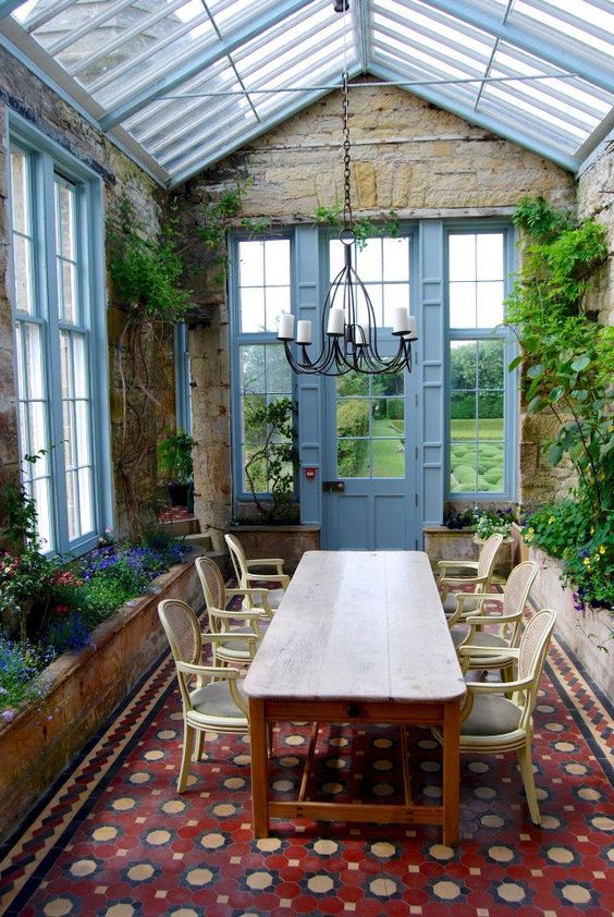 a vintage sunroom with a large carpet, a wooden table and refined chairs, potted greenery and blooms