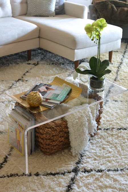 an acrylic coffee table with a basket for storage and some books under the top is a cool idea