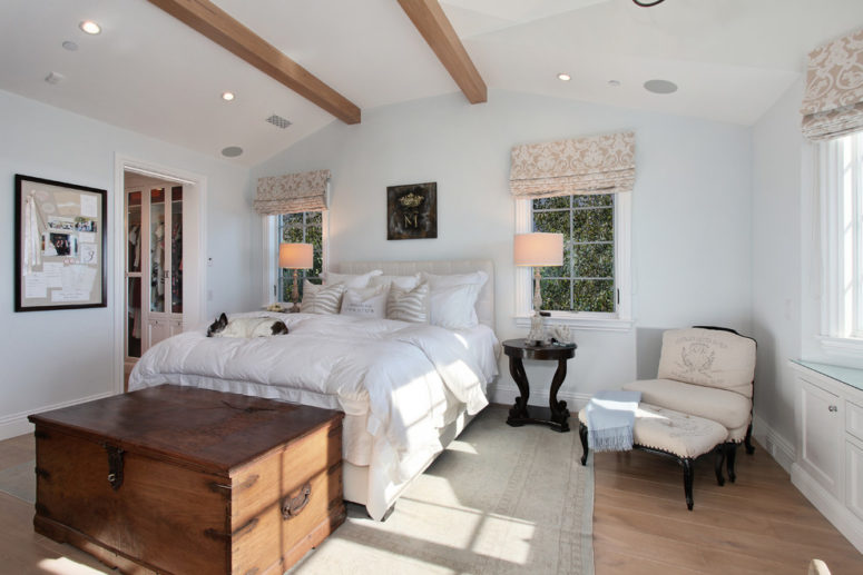 a vintage farmhouse bedroom with light-colored walls, wooden beams, floral curtains and a large chest  (Jeri Koegel Photography)