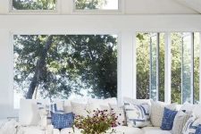 a beautiful modern coastal farmhouse sunroom with a large sectional, blue pillows, a wooden table and woven chandelier