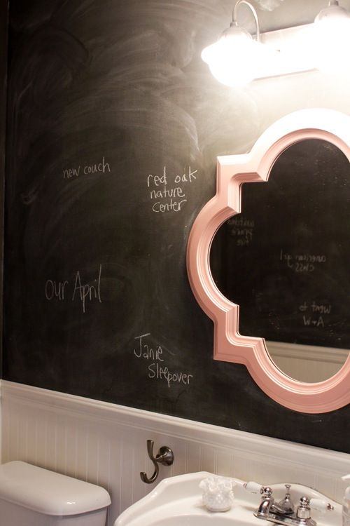 a black and white bathroom with chalkboard walls, white paneling, a mirror in a pink frame and white appliances