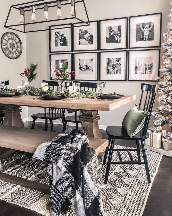 a bright and contrasting dining area with a wooden dining set, black chairs, a black frame and bulb chandelier and a gallery wall