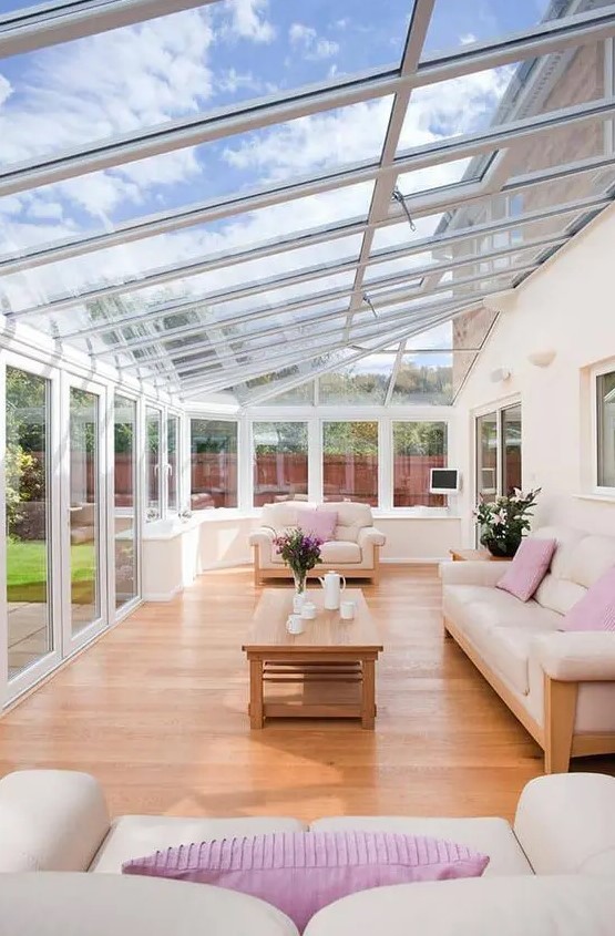 a bright modern attic sunroom with neutral sofas and pink pillows, a wooden table and some teaware is very welcoming