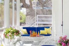 a bright modern beachy sunroom with white metal furniture with super bold upholstery, some potted blooms and seashells