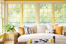 a bright modern farmhouse sunroom with sunny yellow window framing, wicker furniture, a vintage chandelier is very welcoming