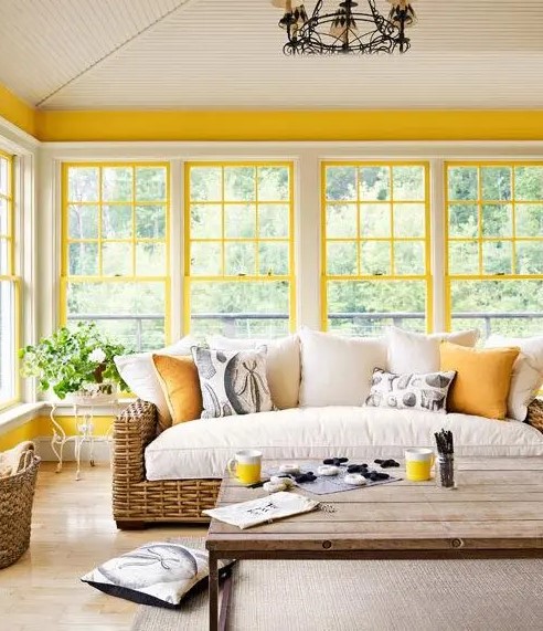 a bright modern farmhouse sunroom with sunny yellow window framing, wicker furniture, a vintage chandelier is very welcoming