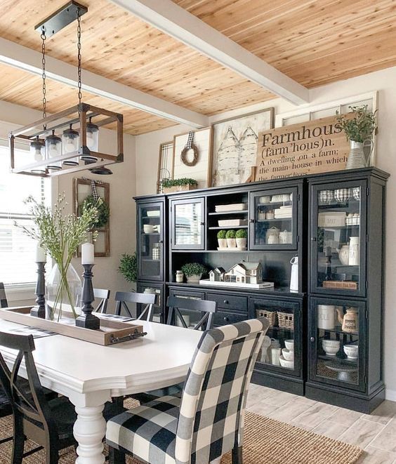 a chic farmhouse dining area with a black and glass buffet, signs, a white table and checked chairs and a frame chandelier