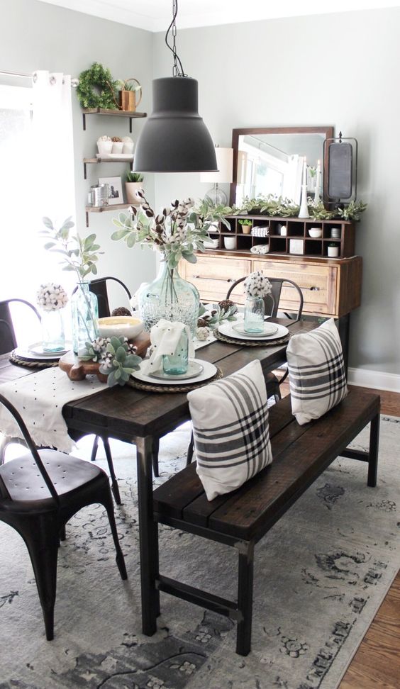 a chic farmhouse dining space with a wooden buffet, a dark stained wooden dining set, a metal lamp and lots of greenery