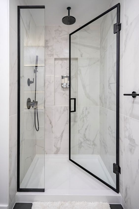 a chic shower space wiht large scale marble tiles, black frame glass doors and black fixtures is a lovely and cool space