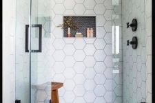 a chic shower space with black penny and white hex tiles, seamless glass doors with a black handle and black fixtures