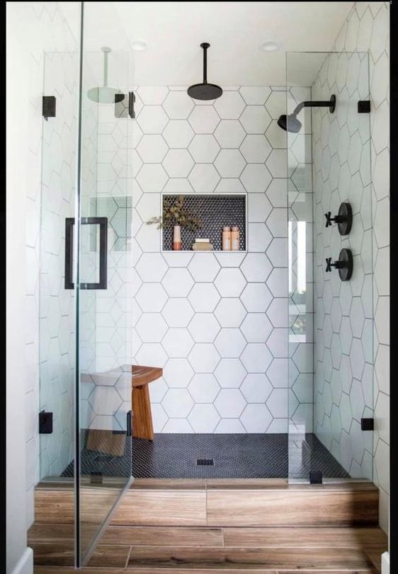 a chic shower space with black penny and white hex tiles, seamless glass doors with a black handle and black fixtures