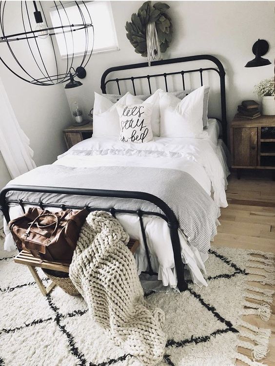 a contemporary farmhouse bedroom in neutrals, with a black metal bed, a metal sphere chandelier, a boho rug and a wreath