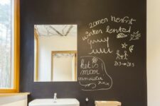 a cool powder room with a black chalkboard accent wall, a wall-mounted sink, a small shelf and a mirror