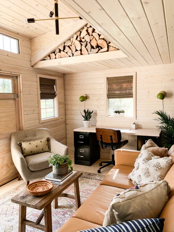 a cozy farmhouse home office with a leather sofa, a cool chair, a contrasting desk and everything around clad with wood